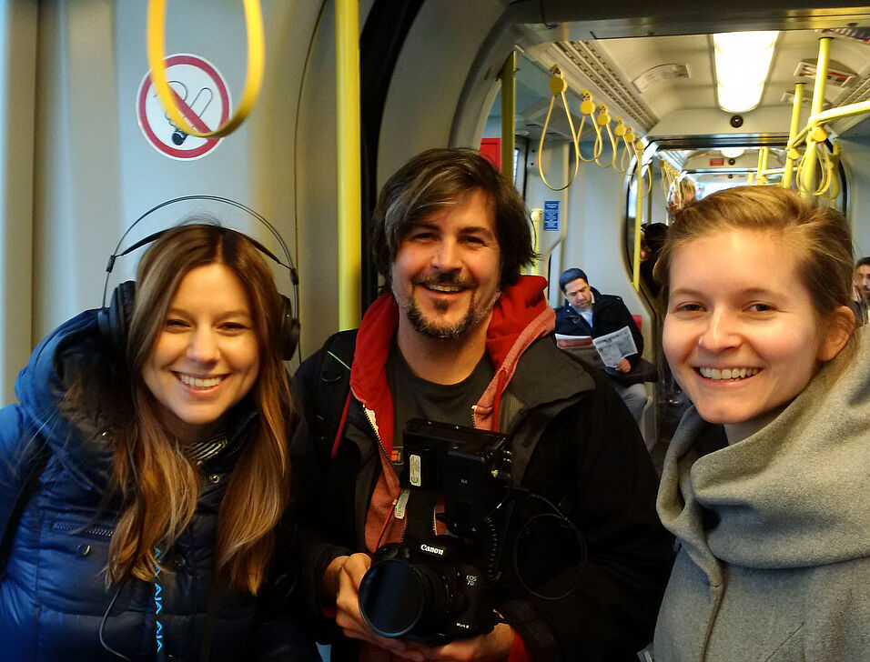 Three people smile at the camera in the tram.