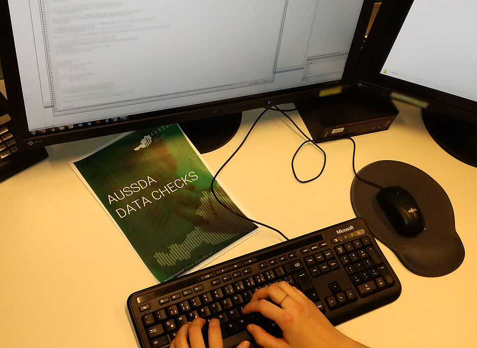 Hands typing on a computer keyboard. Above the keyboard is a folder with "AUSSDA Data Checks" written on it.